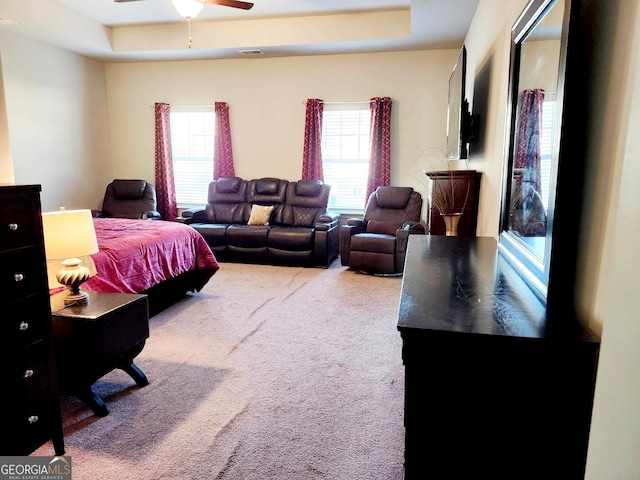 bedroom featuring ceiling fan, carpet floors, a tray ceiling, and multiple windows