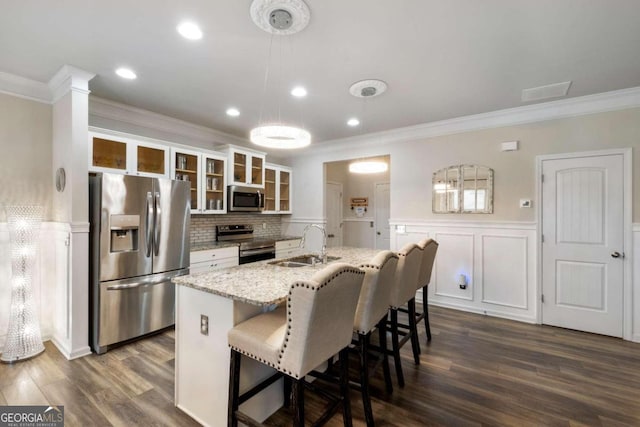 kitchen with light stone counters, a center island with sink, appliances with stainless steel finishes, and crown molding