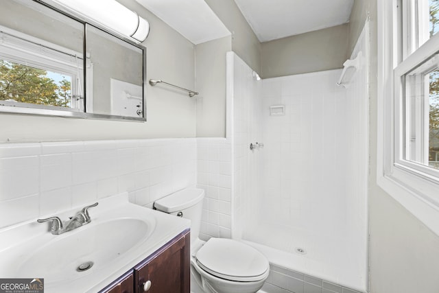 bathroom with vanity, tile walls, toilet, and tiled shower