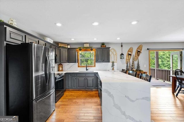 kitchen with black electric range, kitchen peninsula, light hardwood / wood-style flooring, gray cabinetry, and stainless steel fridge