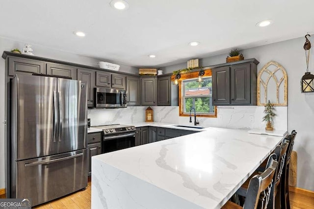 kitchen featuring light stone countertops, a kitchen bar, sink, and stainless steel appliances