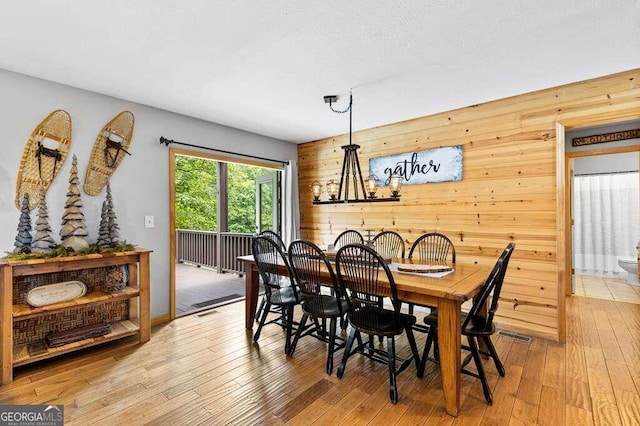 dining space featuring light hardwood / wood-style flooring, a chandelier, and wood walls