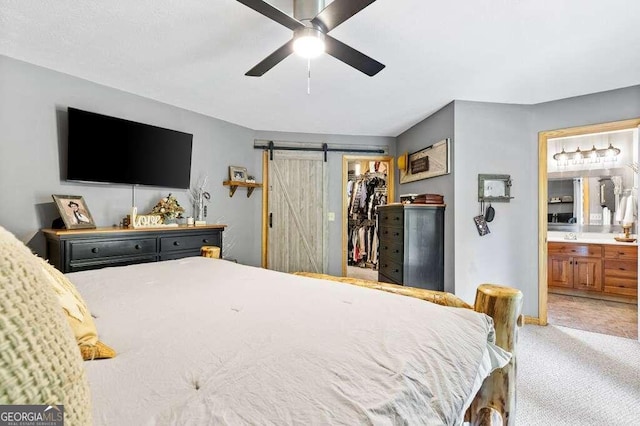 carpeted bedroom featuring a closet, a barn door, ensuite bathroom, a spacious closet, and ceiling fan