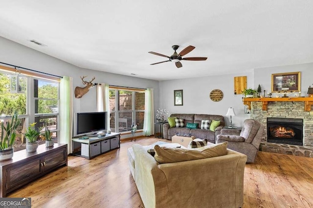 living room with a stone fireplace, ceiling fan, and light hardwood / wood-style flooring