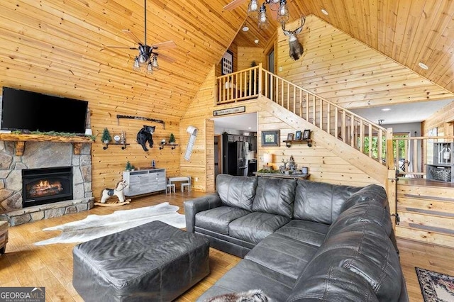 living room featuring high vaulted ceiling, a stone fireplace, ceiling fan, wooden walls, and hardwood / wood-style floors