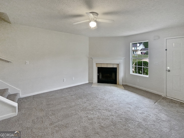 unfurnished living room featuring a tiled fireplace, ceiling fan, light colored carpet, and a textured ceiling