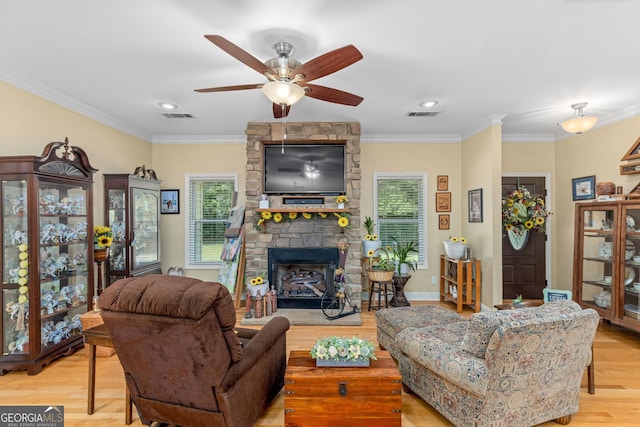 living room with ornamental molding, a stone fireplace, ceiling fan, and light hardwood / wood-style flooring