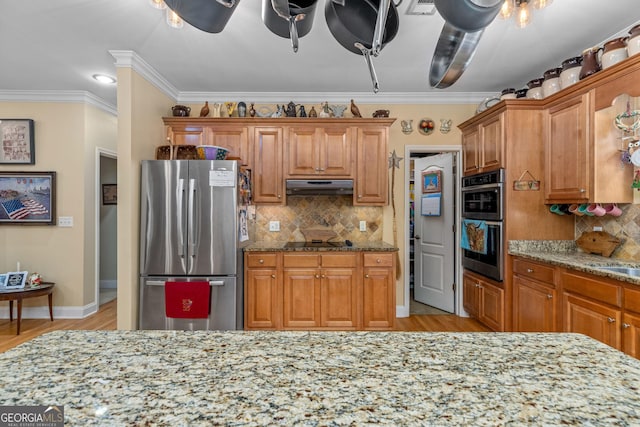 kitchen with appliances with stainless steel finishes, light stone counters, ornamental molding, light hardwood / wood-style floors, and decorative backsplash