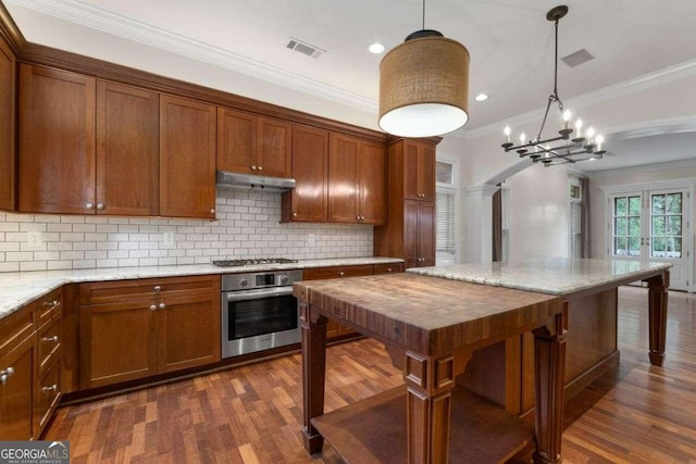 kitchen with pendant lighting, dark wood-type flooring, decorative backsplash, appliances with stainless steel finishes, and ornamental molding