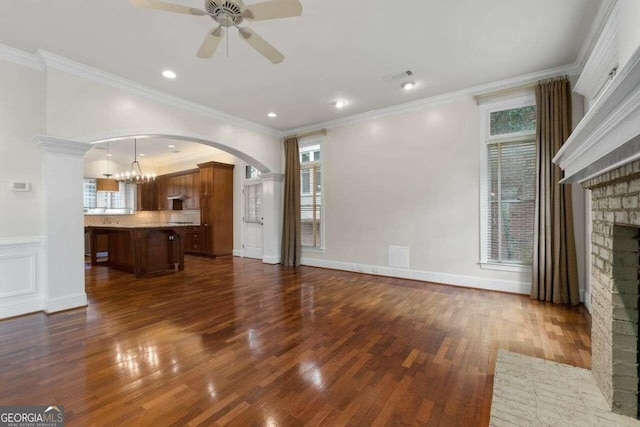 unfurnished living room with a healthy amount of sunlight, dark wood-type flooring, ceiling fan with notable chandelier, and a fireplace