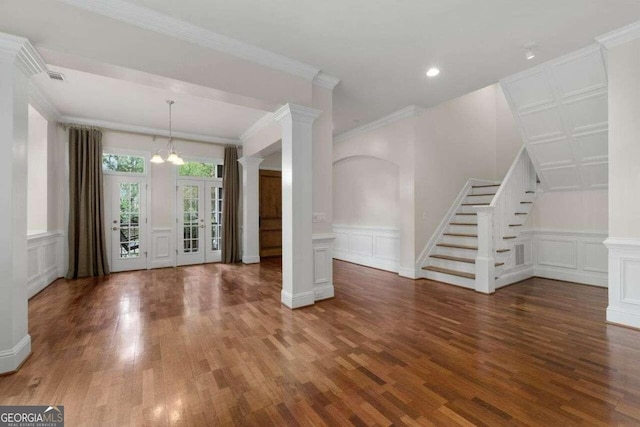 foyer entrance with crown molding, decorative columns, dark wood-type flooring, and a chandelier