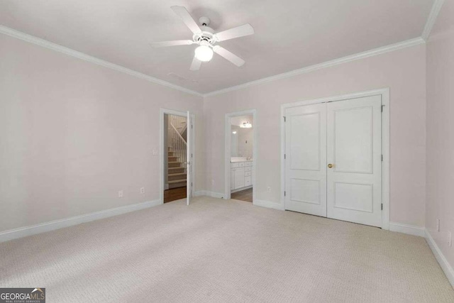 unfurnished bedroom featuring a closet, light carpet, ensuite bathroom, crown molding, and ceiling fan