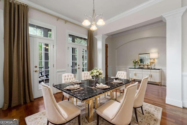 dining area with dark wood-type flooring, ornate columns, an inviting chandelier, french doors, and ornamental molding