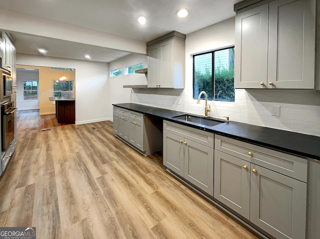 kitchen featuring backsplash, a sink, dark countertops, light wood finished floors, and wall oven