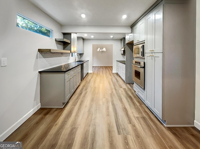 kitchen featuring a sink, open shelves, light wood finished floors, appliances with stainless steel finishes, and dark countertops