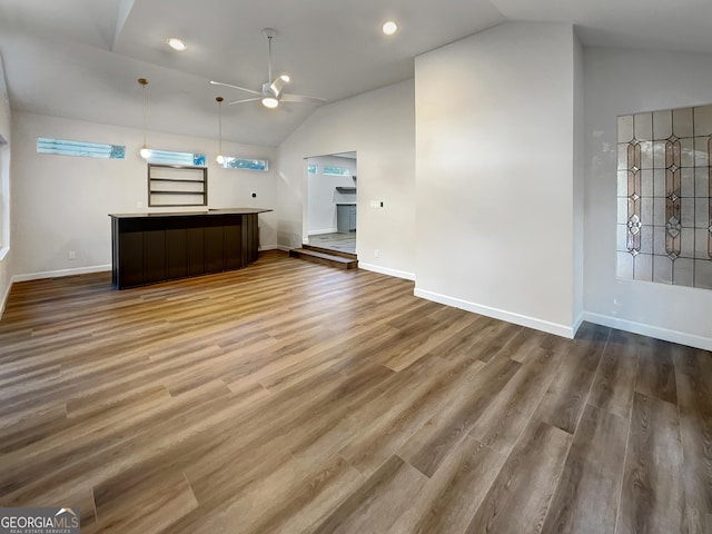 unfurnished living room with a ceiling fan, baseboards, vaulted ceiling, and wood finished floors