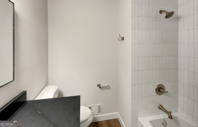 bathroom featuring wood-type flooring, tiled shower / bath combo, and toilet