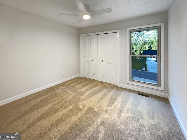 unfurnished bedroom with a closet, ceiling fan, carpet flooring, and a textured ceiling