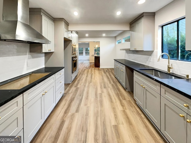 kitchen featuring wall chimney exhaust hood, dark countertops, appliances with stainless steel finishes, a sink, and light wood-type flooring