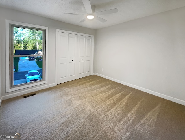 unfurnished bedroom with a closet, ceiling fan, carpet flooring, and a textured ceiling