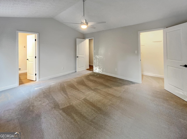 unfurnished bedroom with ensuite bathroom, carpet, baseboards, lofted ceiling, and a walk in closet