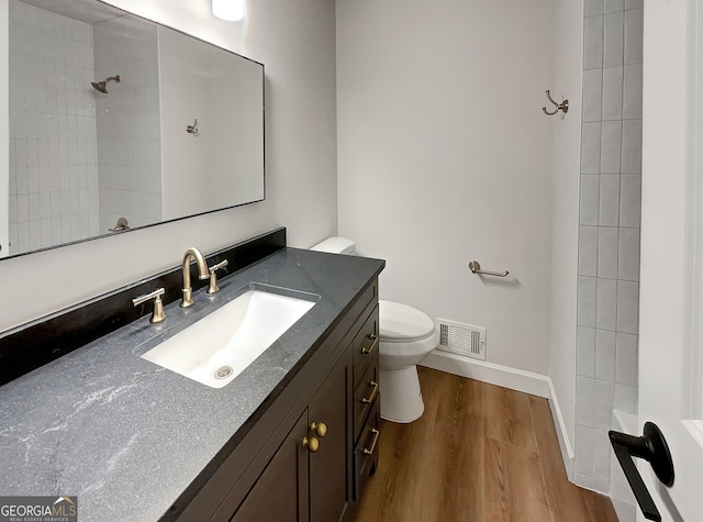 bathroom with hardwood / wood-style floors, a tile shower, vanity, and toilet