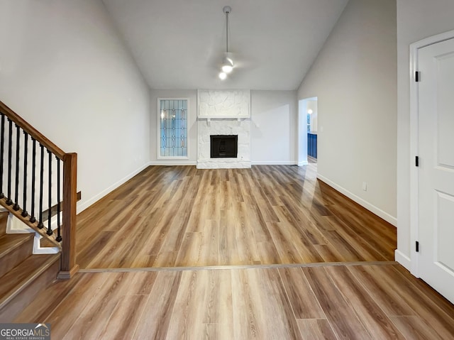 unfurnished living room featuring stairway, a fireplace, wood finished floors, lofted ceiling, and baseboards