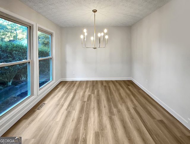 unfurnished dining area featuring an inviting chandelier, wood-type flooring, and a textured ceiling