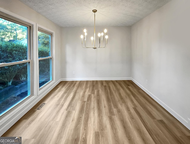 unfurnished dining area with baseboards, a notable chandelier, and wood finished floors