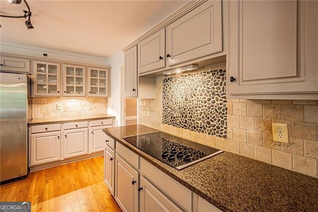 kitchen featuring light hardwood / wood-style floors, tasteful backsplash, stainless steel refrigerator, black electric cooktop, and ornamental molding