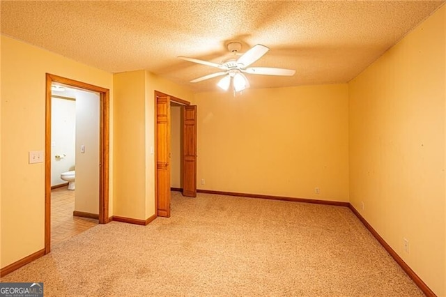 unfurnished bedroom with a textured ceiling, connected bathroom, ceiling fan, and light colored carpet