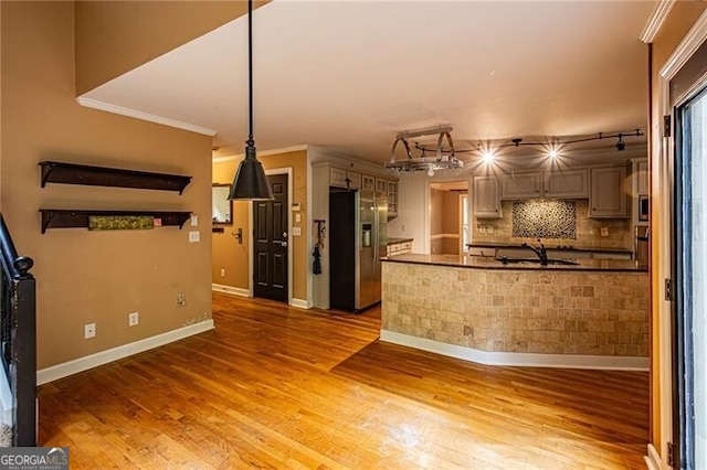 kitchen with ornamental molding, wood-type flooring, hanging light fixtures, and stainless steel fridge with ice dispenser