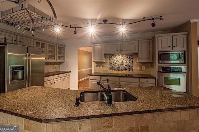 kitchen featuring dark stone counters, built in appliances, sink, a center island with sink, and crown molding