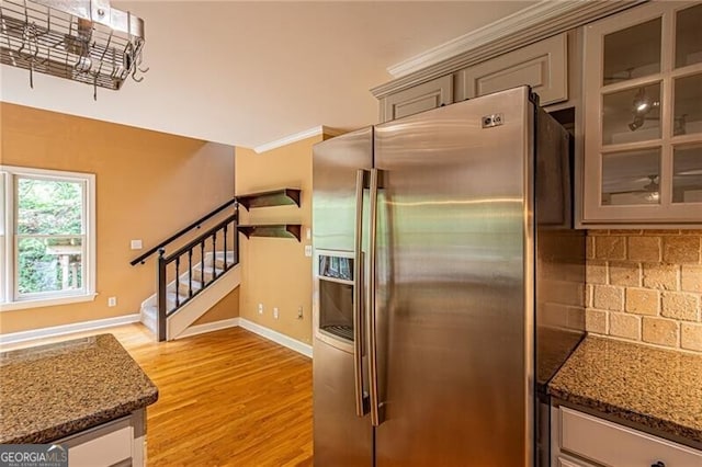 kitchen with dark stone counters, tasteful backsplash, light hardwood / wood-style flooring, ornamental molding, and stainless steel fridge