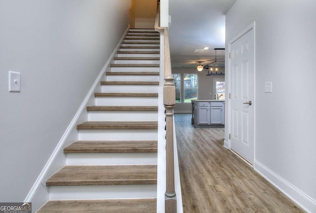 stairs with baseboards, wood finished floors, and ceiling fan