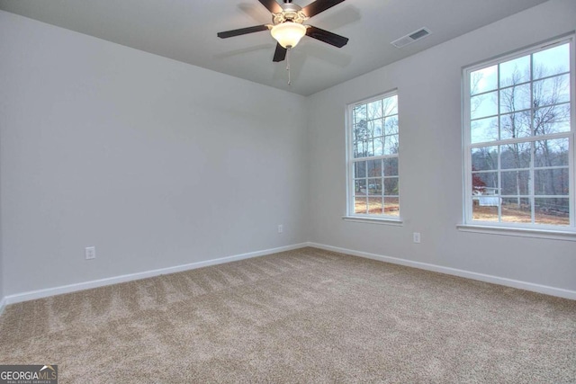 carpeted spare room featuring baseboards, visible vents, and ceiling fan