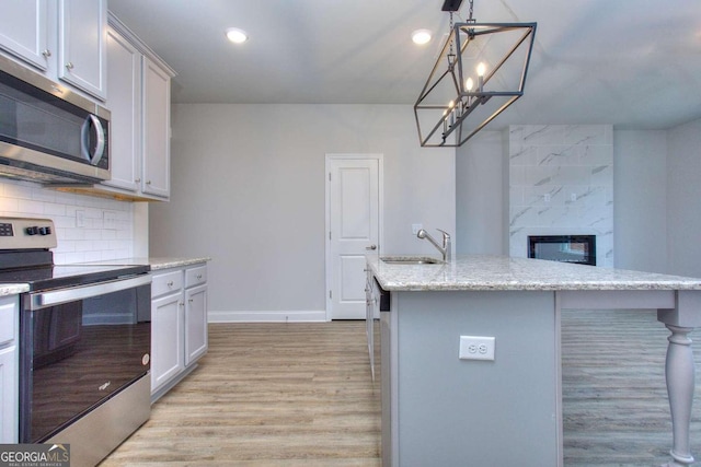 kitchen featuring tasteful backsplash, light wood-style flooring, a sink, appliances with stainless steel finishes, and baseboards