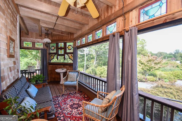 sunroom featuring wood ceiling, beam ceiling, ceiling fan, and a healthy amount of sunlight