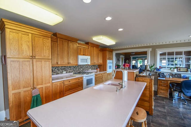 kitchen featuring built in desk, decorative backsplash, white appliances, a kitchen island with sink, and sink