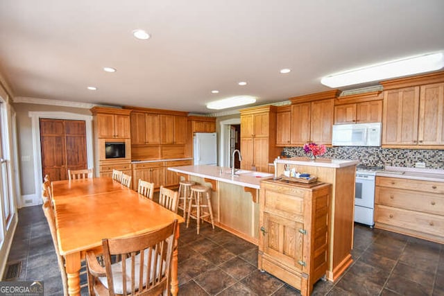 kitchen featuring tasteful backsplash, sink, an island with sink, a breakfast bar area, and white appliances