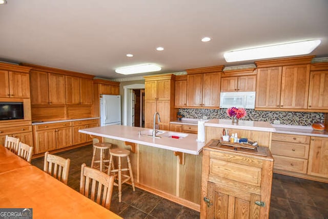 kitchen featuring an island with sink, sink, white appliances, backsplash, and a breakfast bar area