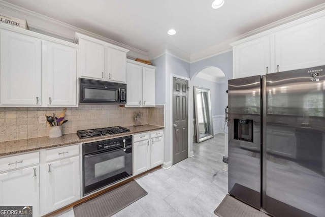 kitchen with ornamental molding, backsplash, white cabinetry, black appliances, and dark stone counters