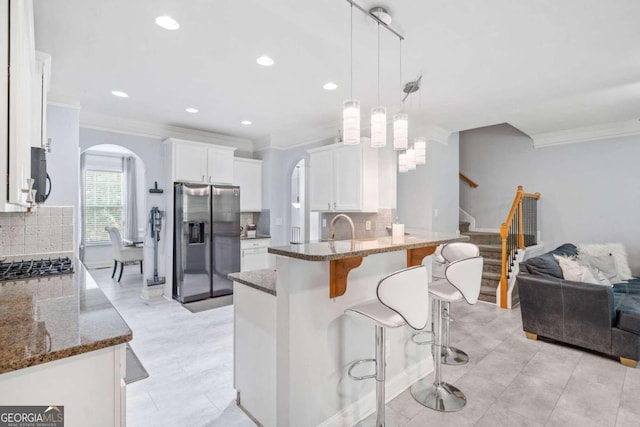 kitchen featuring white cabinetry, kitchen peninsula, backsplash, appliances with stainless steel finishes, and decorative light fixtures