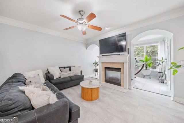 living room with a tile fireplace, light tile patterned floors, crown molding, and ceiling fan