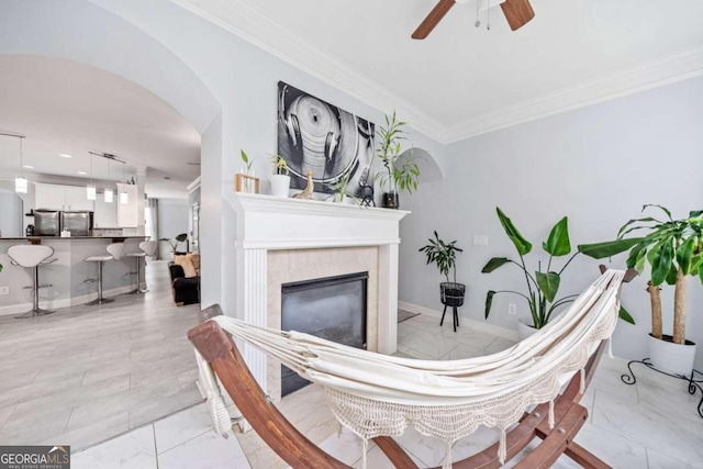 living room featuring ornamental molding, a tiled fireplace, and ceiling fan