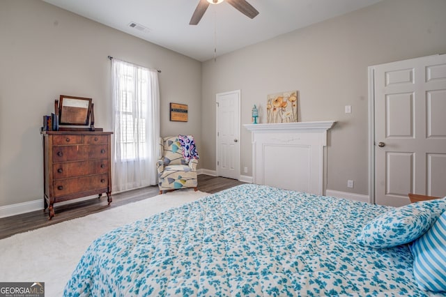 bedroom featuring a fireplace, dark wood-type flooring, and ceiling fan