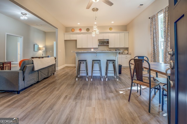 interior space with a kitchen island with sink, white cabinetry, a kitchen bar, light hardwood / wood-style flooring, and ceiling fan