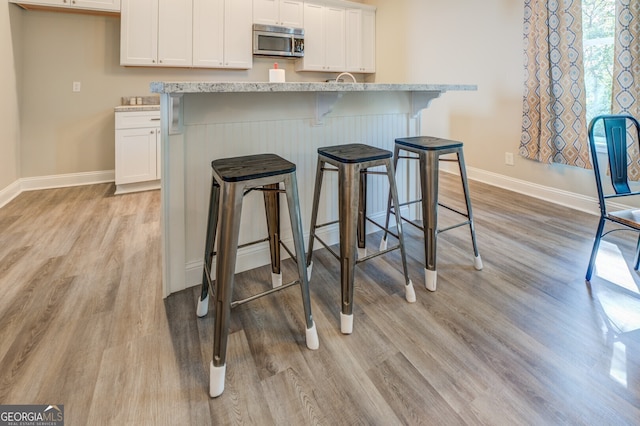 kitchen featuring light stone countertops, white cabinets, light hardwood / wood-style floors, and a kitchen bar