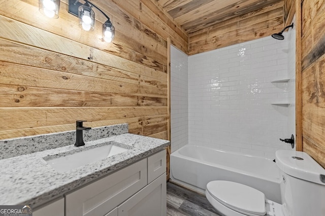 full bathroom featuring tiled shower / bath, vanity, wooden walls, hardwood / wood-style flooring, and toilet