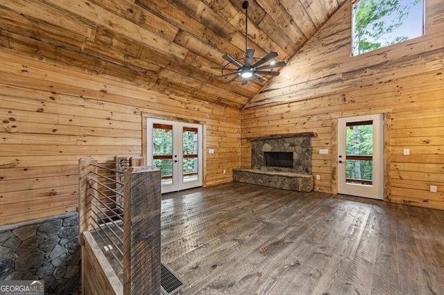 unfurnished living room featuring wood walls, ceiling fan, french doors, and a stone fireplace